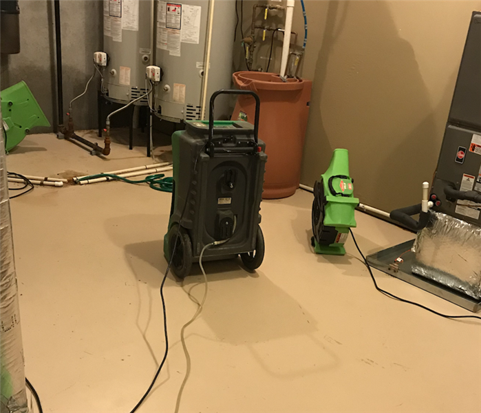 Basement Flooded Around Hot Water Heaters In Corner Of Room With SERVPRO Equipment In Use On Floor.